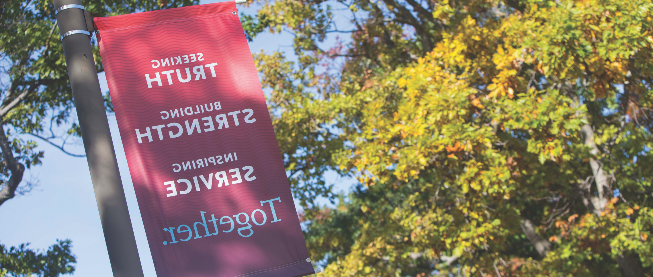 A banner on Campus Drive displays the 博彩网址大全 mission statement: Seeking Truth, 建筑的力量, 鼓舞人心的服务:一起.